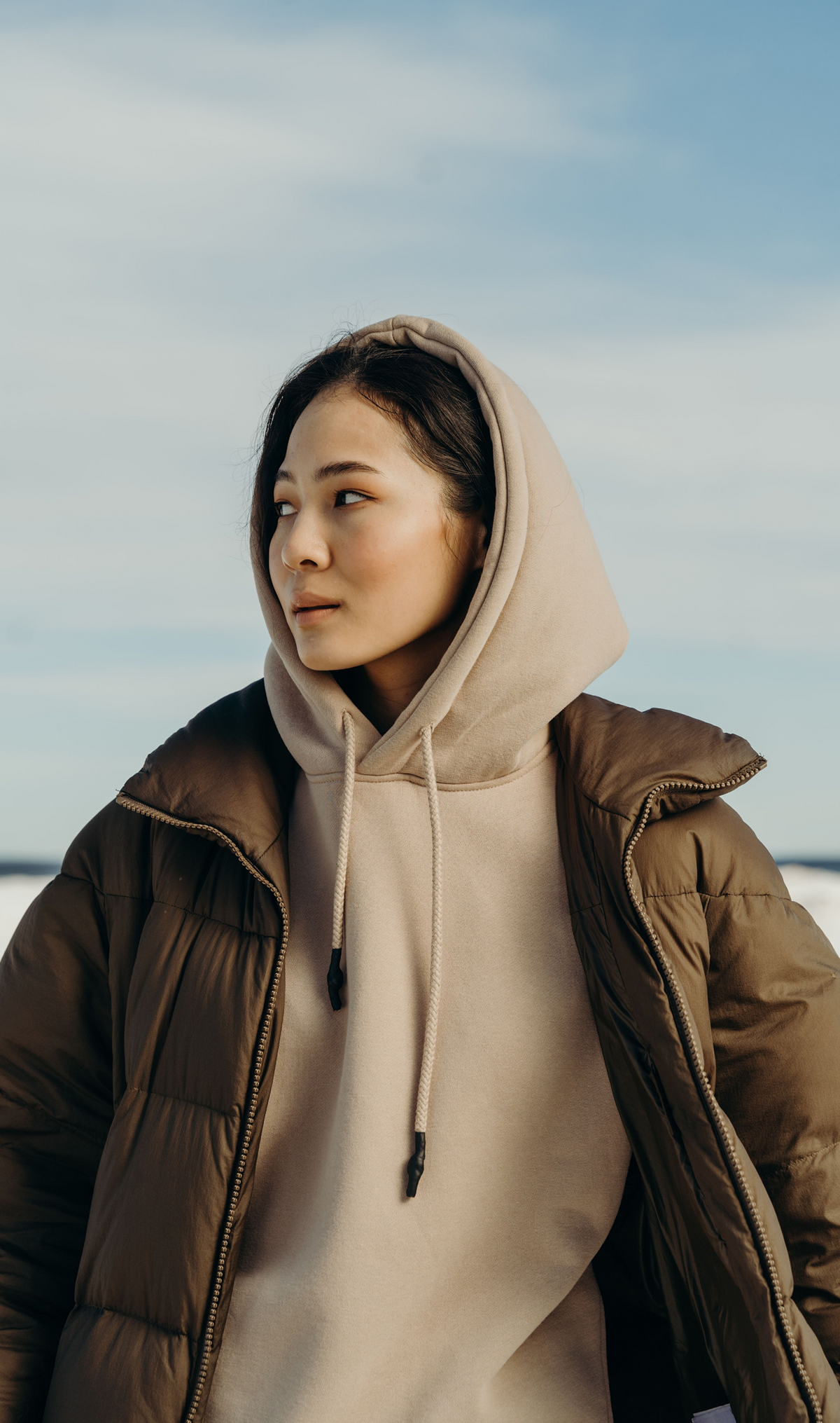 Model wearing an elevated hoodie with a drawstring hood under a puffer jacket