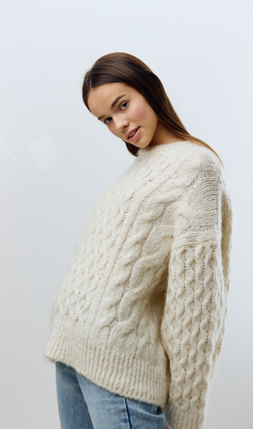 Model wearing a textured cable knit sweater with a relaxed fit